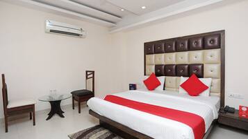 A hotel room with a large bed, a chair, a small table, and an air conditioning unit.