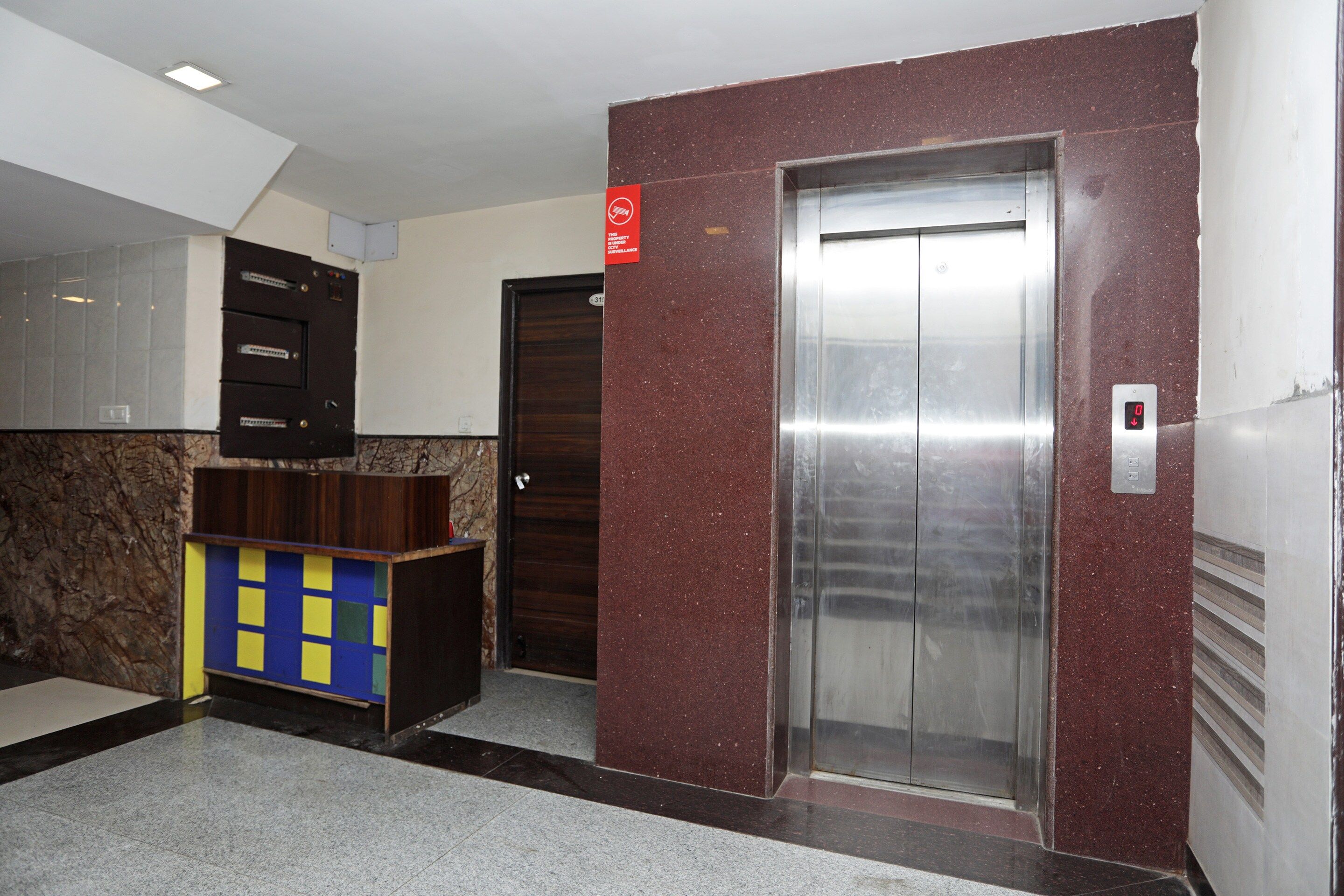 Un ascensor con pantalla digital, una puerta con un letrero rojo y una pared de azulejos.