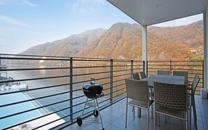 A balcony with a view of a river and mountains, a grill, and a table with chairs. - Casa 32 Resort (Gapyeong-gun)