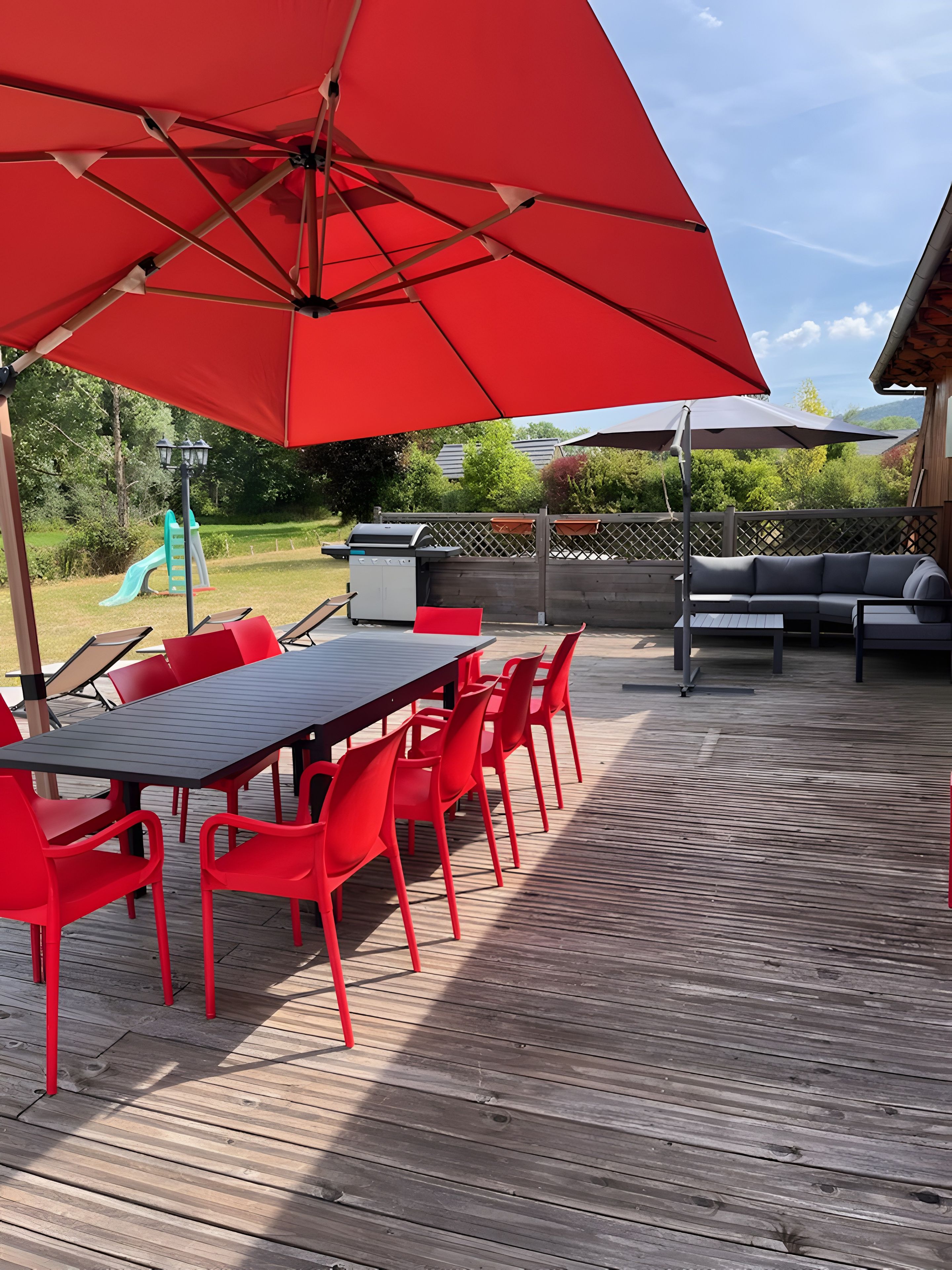 Eine Holzterrasse mit einem roten Tisch und Stühlen, einem Grill und einem überdachten Sitzbereich.