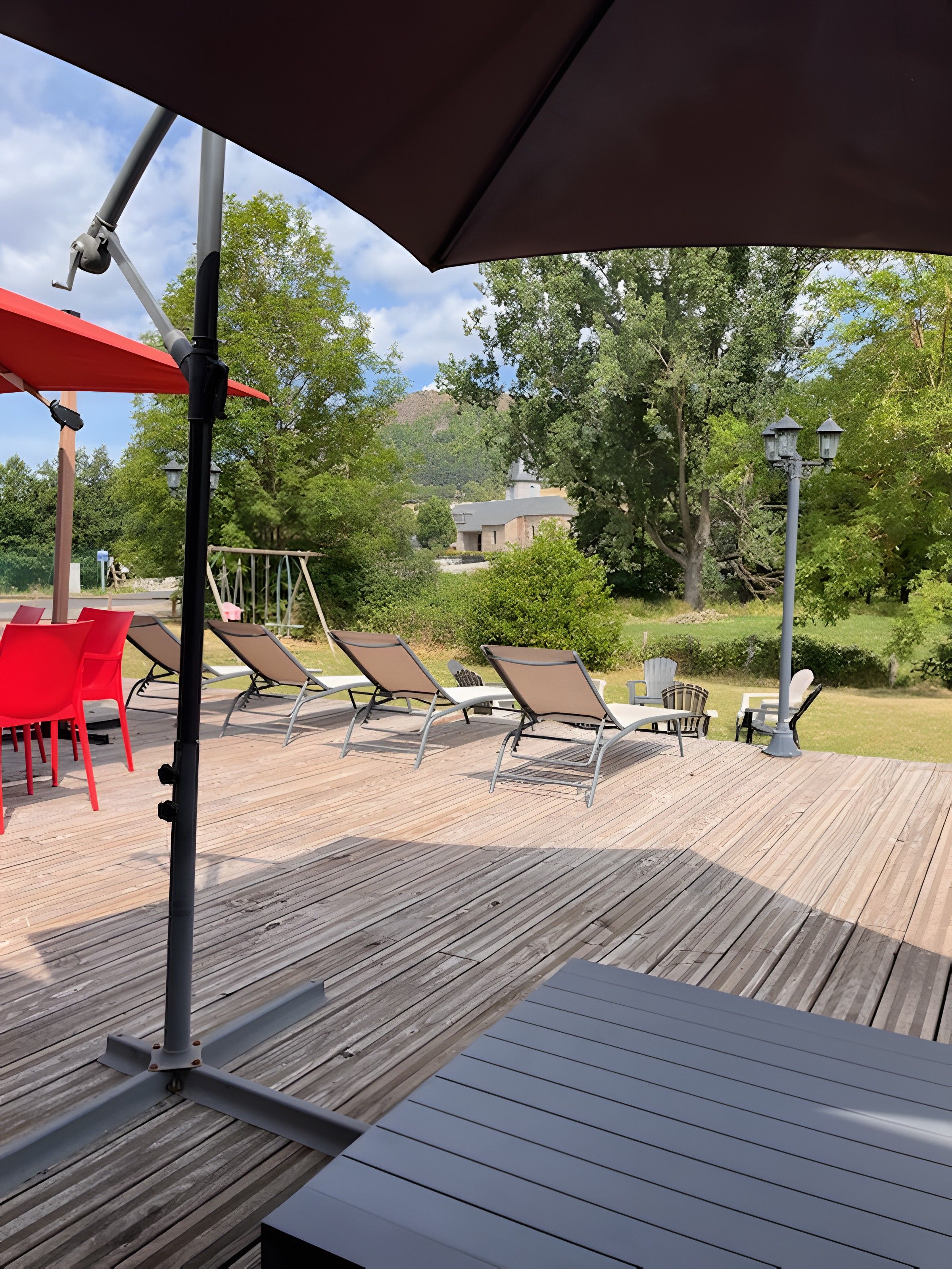 A wooden deck with outdoor seating, including red chairs and brown lounge chairs, and a red umbrella.