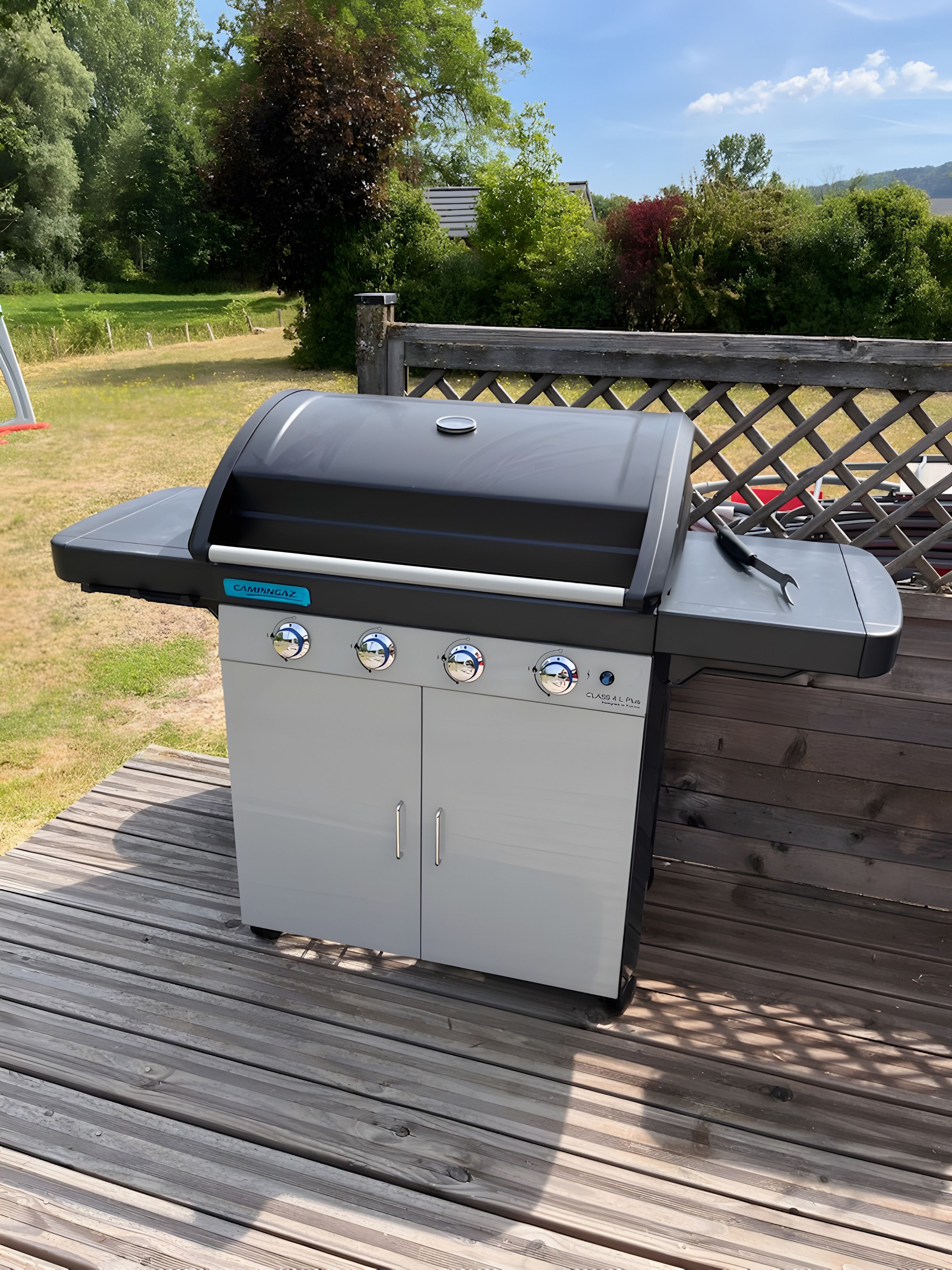 Una barbecue portatile con quattro fuochi, un display digitale e un ripiano laterale, posizionata su un patio in legno.