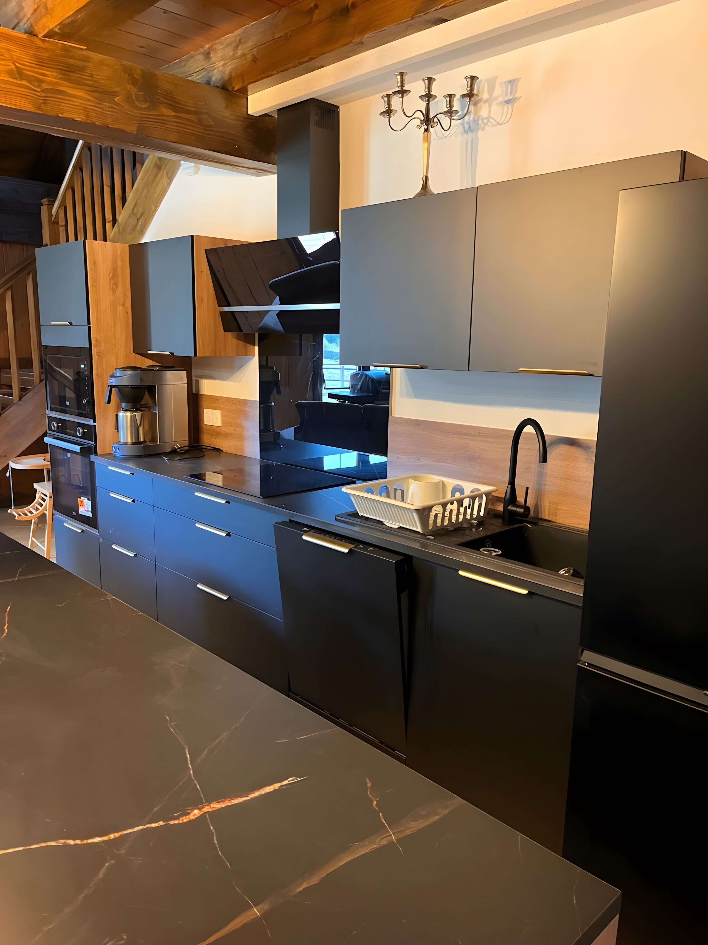 A modern kitchen with black cabinetry, a built-in oven, a coffee maker, and a sink.