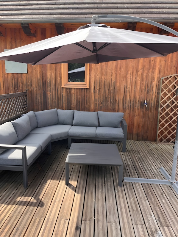 Una terraza de madera con un sofá seccional gris y una mesa de centro blanca.