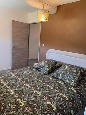 Een slaapkamer met een bed, een deur en een hanglamp.