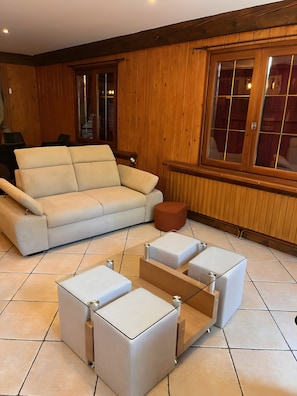 Una sala de estar moderna con un sofá color beige, una mesa de centro de madera y un ventanal con persianas de madera.