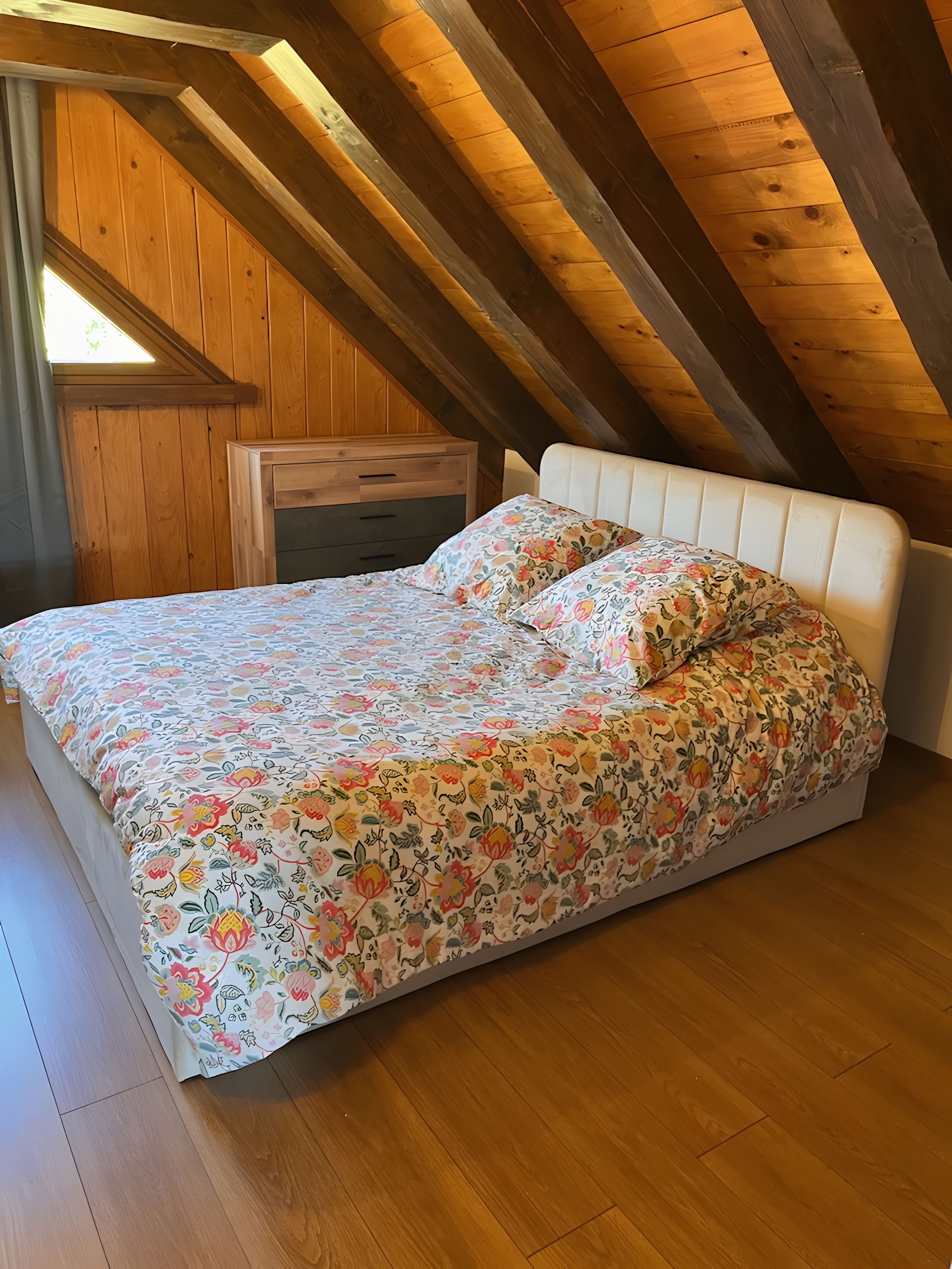 Ein Schlafzimmer mit holzverkleideter Schräge, einem Bett mit Blumenmuster und einer Holzkommode.