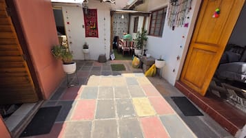 Um pátio com piso de azulejos, plantas em vasos, uma porta de madeira e uma parede decorada.