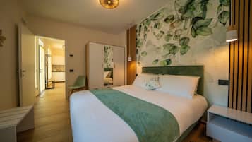 Camera d'hotel con un letto grande, un poggiatesta verde, una parete decorata con un motivo a foglia, un comodino in legno e una porta che conduce al bagno.