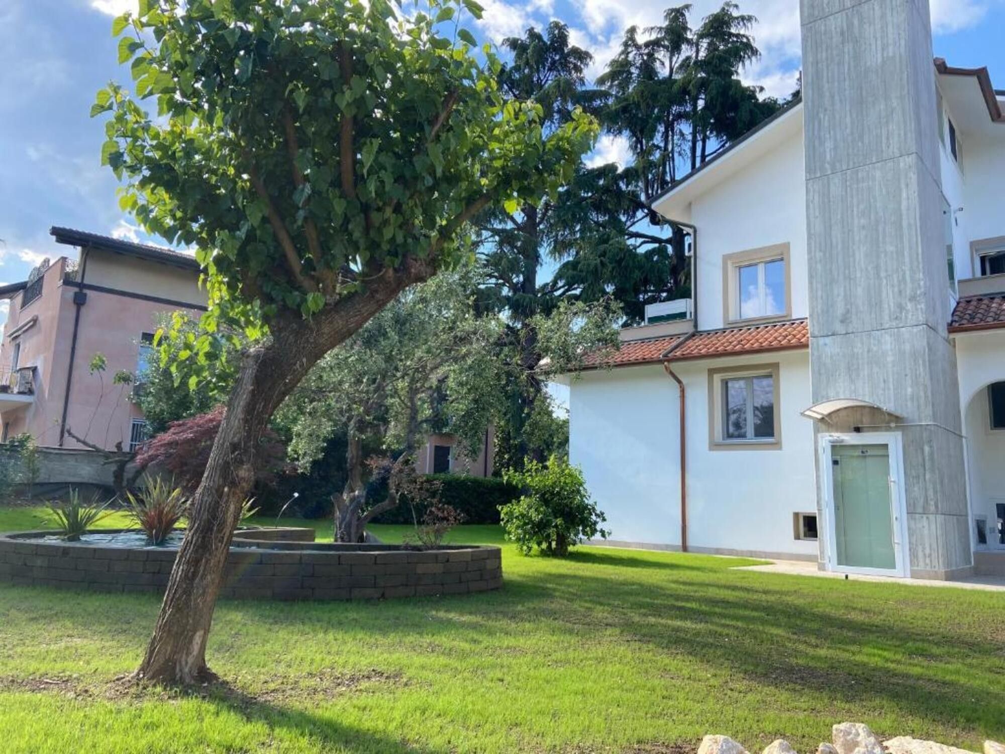 Un edificio residenziale con un grande albero sul davanti, un muro di sostegno in mattoni e un cielo sereno.