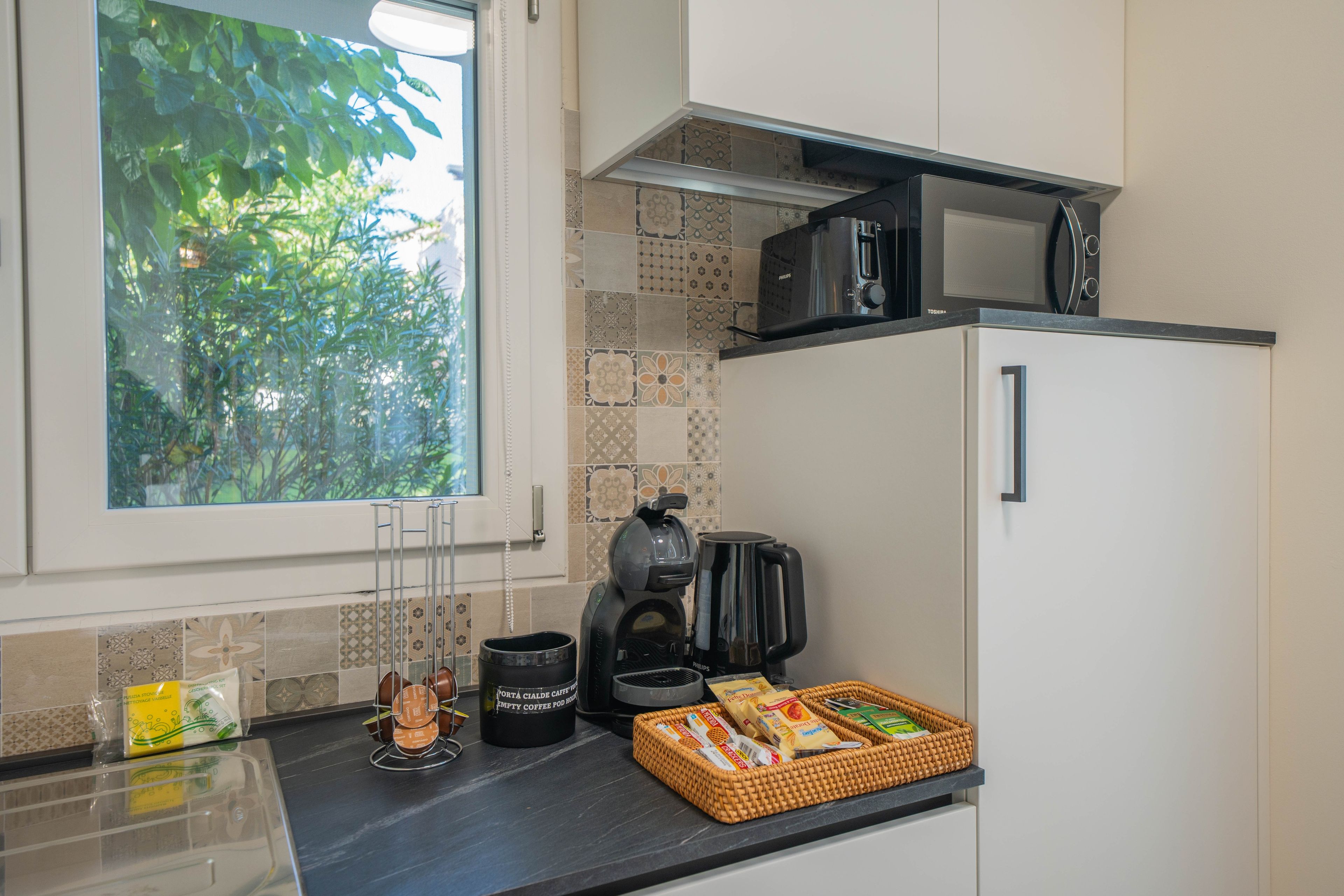 A kitchen with a window, a microwave, a coffee maker, and a basket of bread.