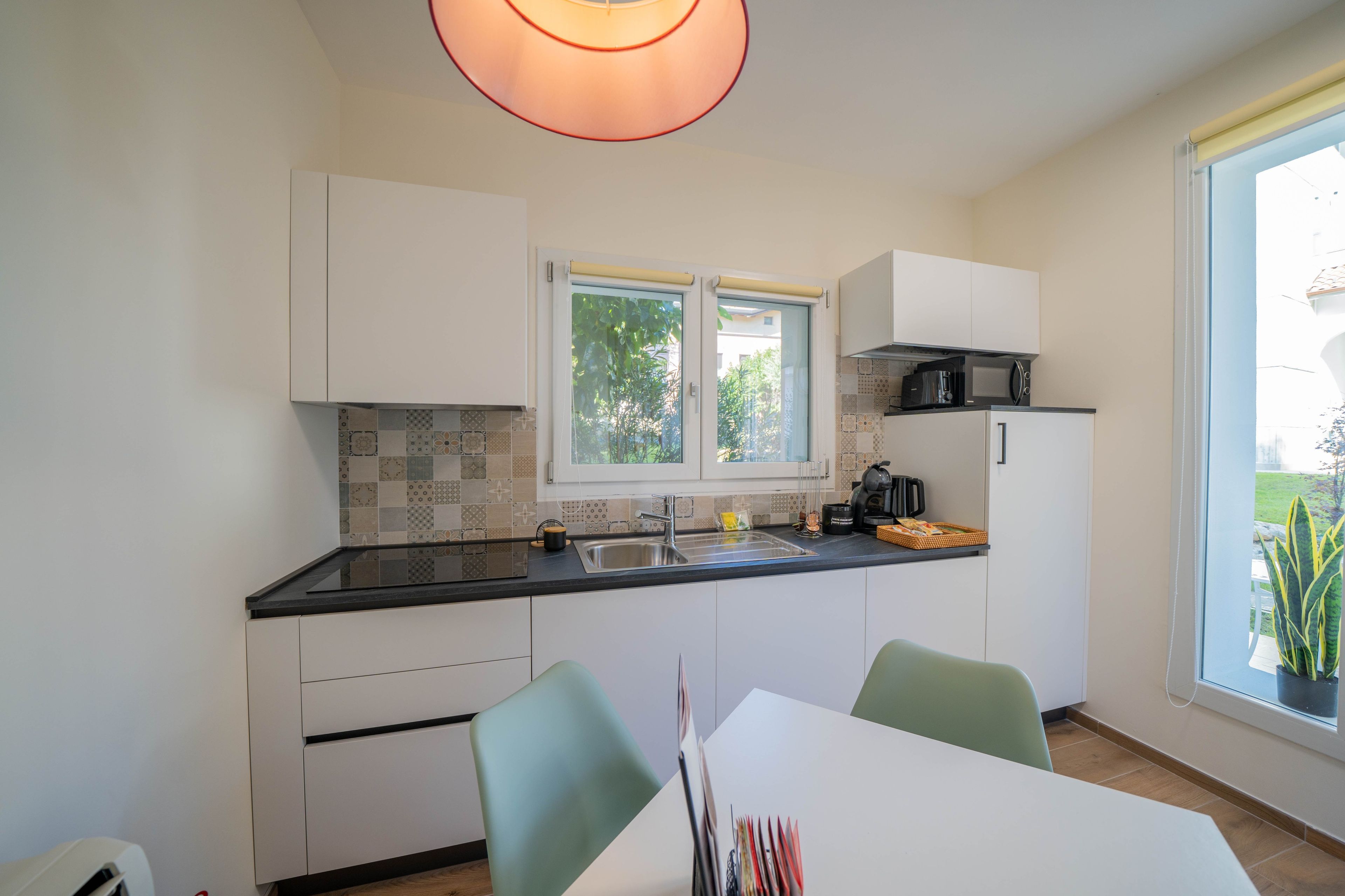 Una cucina moderna con una finestra, mobili bianchi e un'area pranzo con tavolo e sedie.