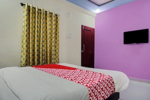 Ein Hotelzimmer mit einem Bett, einem an der Wand befestigten Fernseher, einer Tür und einem Vorhang.