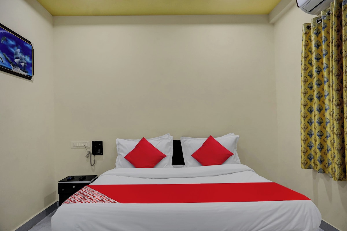 A hotel room with a bed, a bedside table, a phone, and a wall-mounted air conditioner.