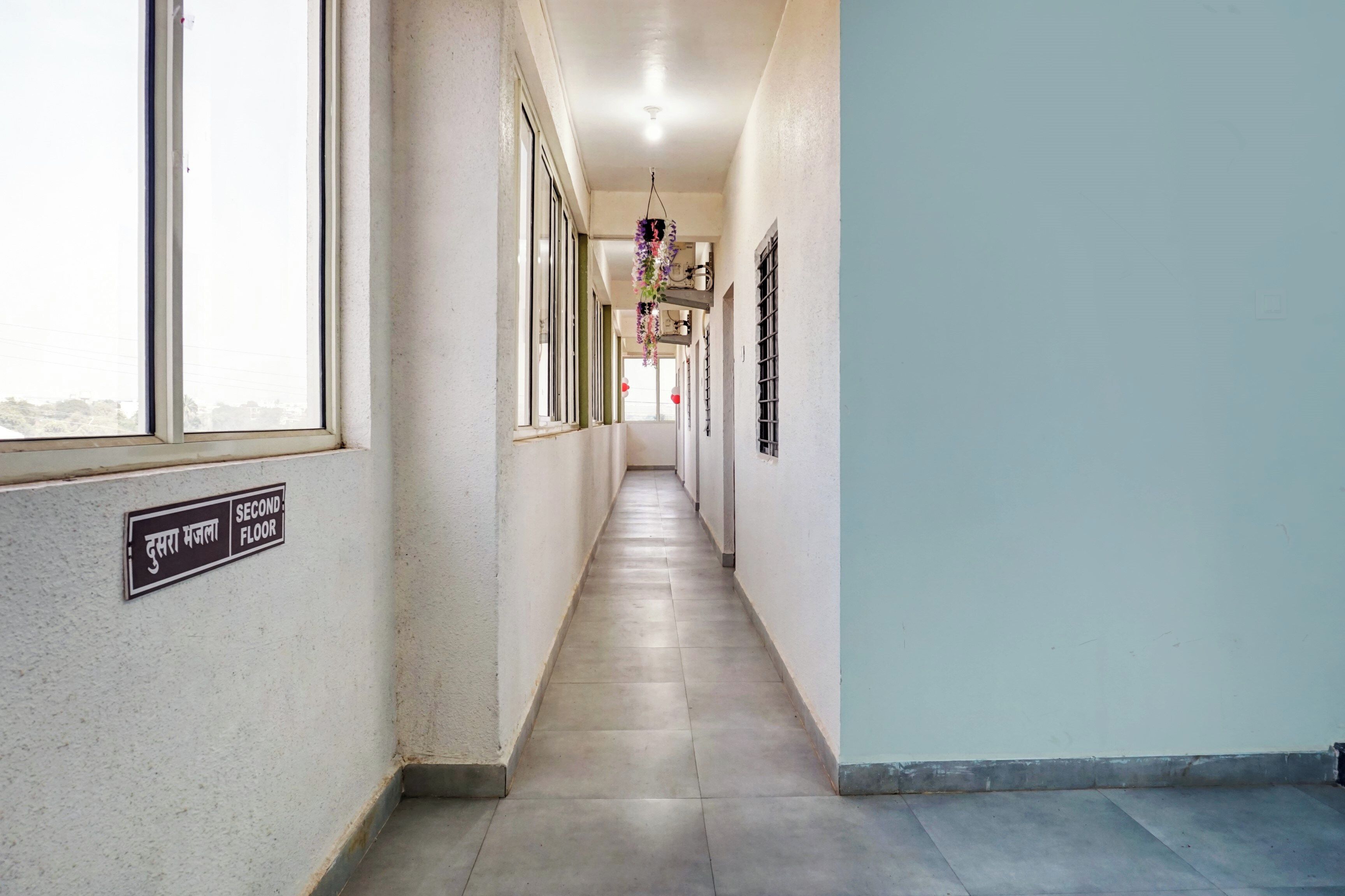 Un pasillo con un letrero que indica el segundo piso, una decoración floral colgante y una ventana a la izquierda.