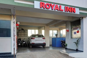 Entrada del Royal Inn con un coche blanco estacionado en su interior, un mostrador de recepción y un cartel con el número de recepción.