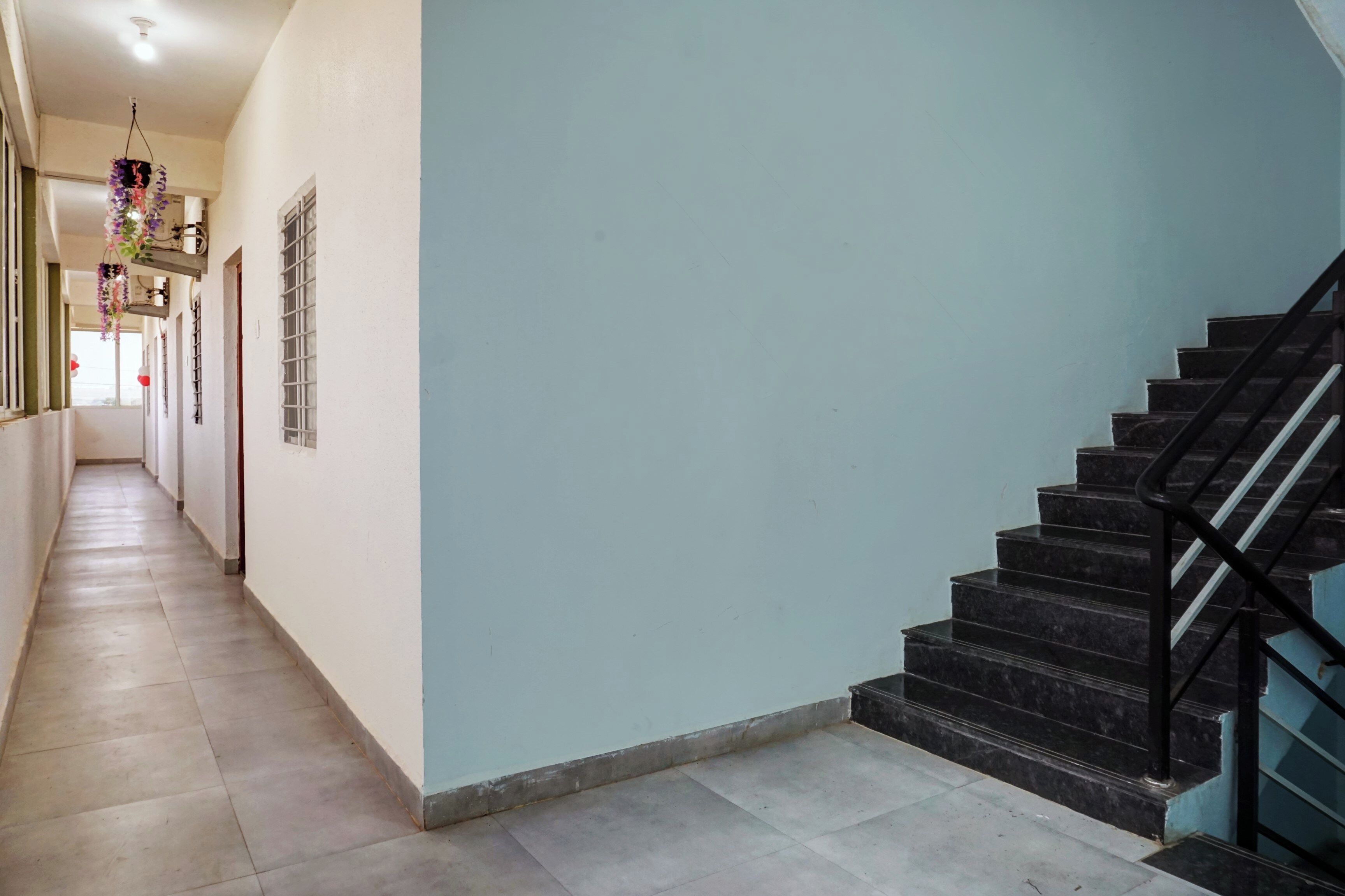 A corridor with a staircase on the right, a hanging decoration, and a window with bars.