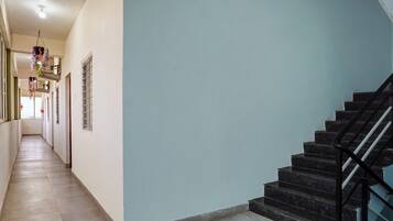 A corridor with a staircase on the right, a hanging decoration, and a window with bars.