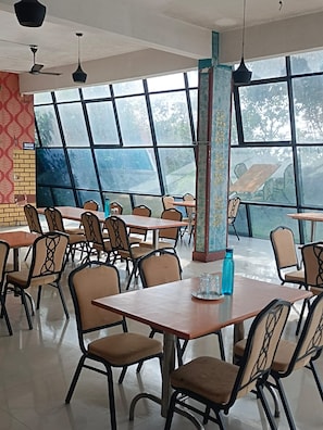 Un vaste espace de restauration intérieur, doté de nombreuses tables et chaises, de grandes fenêtres et de ventilateurs de plafond.