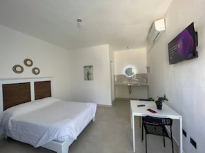 Habitació d'hotel amb un llit, escriptori, cadira, mirall i televisió penjada a la paret.