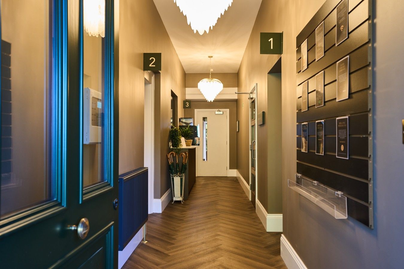 A hotel hallway with numbered doors, a chandelier, and a wall-mounted display.