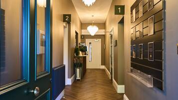 A hotel hallway with numbered doors, a chandelier, and a wall-mounted display.
