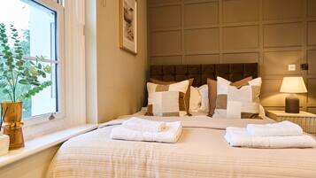 A hotel room with a large bed, a bedside table with a lamp, a window with a plant, and a wall-mounted artwork.