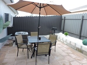 En udendørs patio med et bord, stole, grill og en stor parasol.