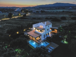Une maison moderne à deux étages, dotée d’une piscine, entourée de vastes champs et située à proximité de montagnes lointaines.