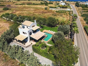 Une grande maison avec une piscine, entourée de verdure et bordée par une route.