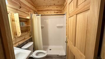 A wooden-paneled bathroom with a toilet, sink, and shower stall.