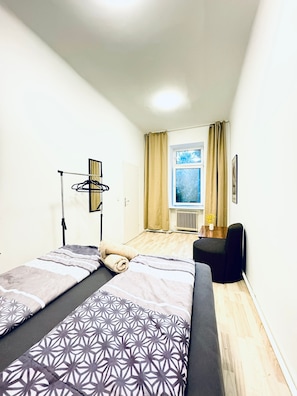 Une petite pièce bien éclairée, avec un lit, une chaise et une fenêtre avec des rideaux.