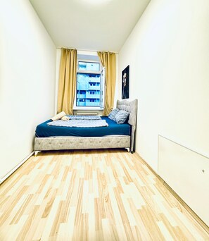 Une chambre à coucher avec un lit, une fenêtre avec des rideaux et un radiateur.