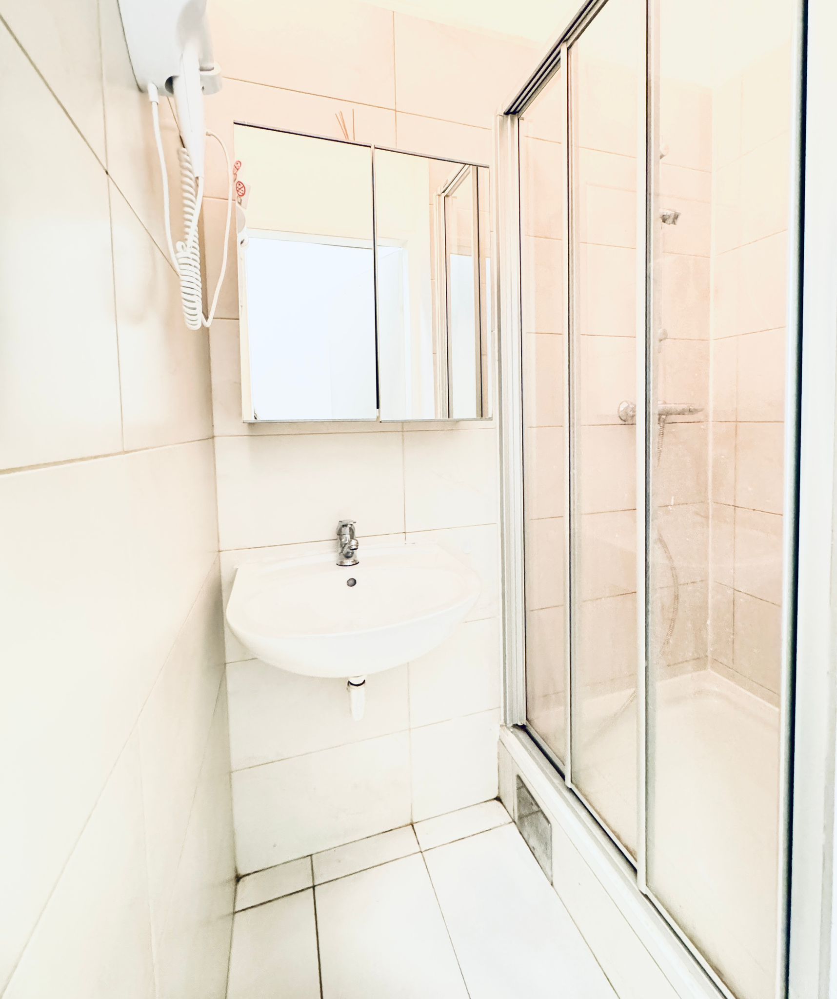 Ein Badezimmer mit weißem Waschbecken, einem Spiegel und einer Duschkabine aus Glas.