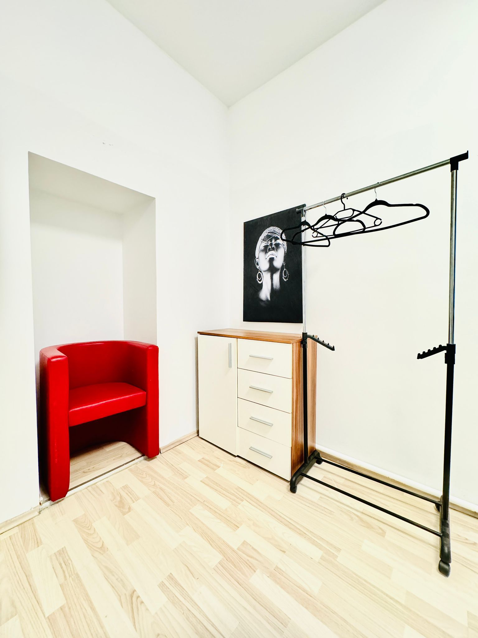 Una habitación con una silla roja, un armario blanco y una obra de arte blanco y negro en la pared.