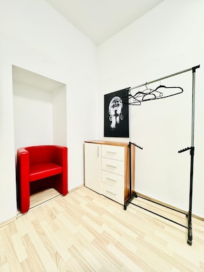 Una habitación con una silla roja, un armario blanco y una obra de arte blanco y negro en la pared.