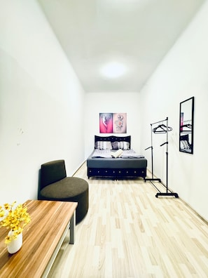Une petite chambre moderne, avec un lit, une chaise, une table ornée de fleurs et un miroir au mur.