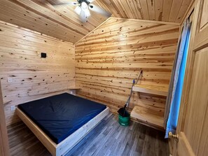 Quarto pequeno de cabana de madeira, com uma cama de solteiro, um ventilador de teto e uma porta para o exterior.