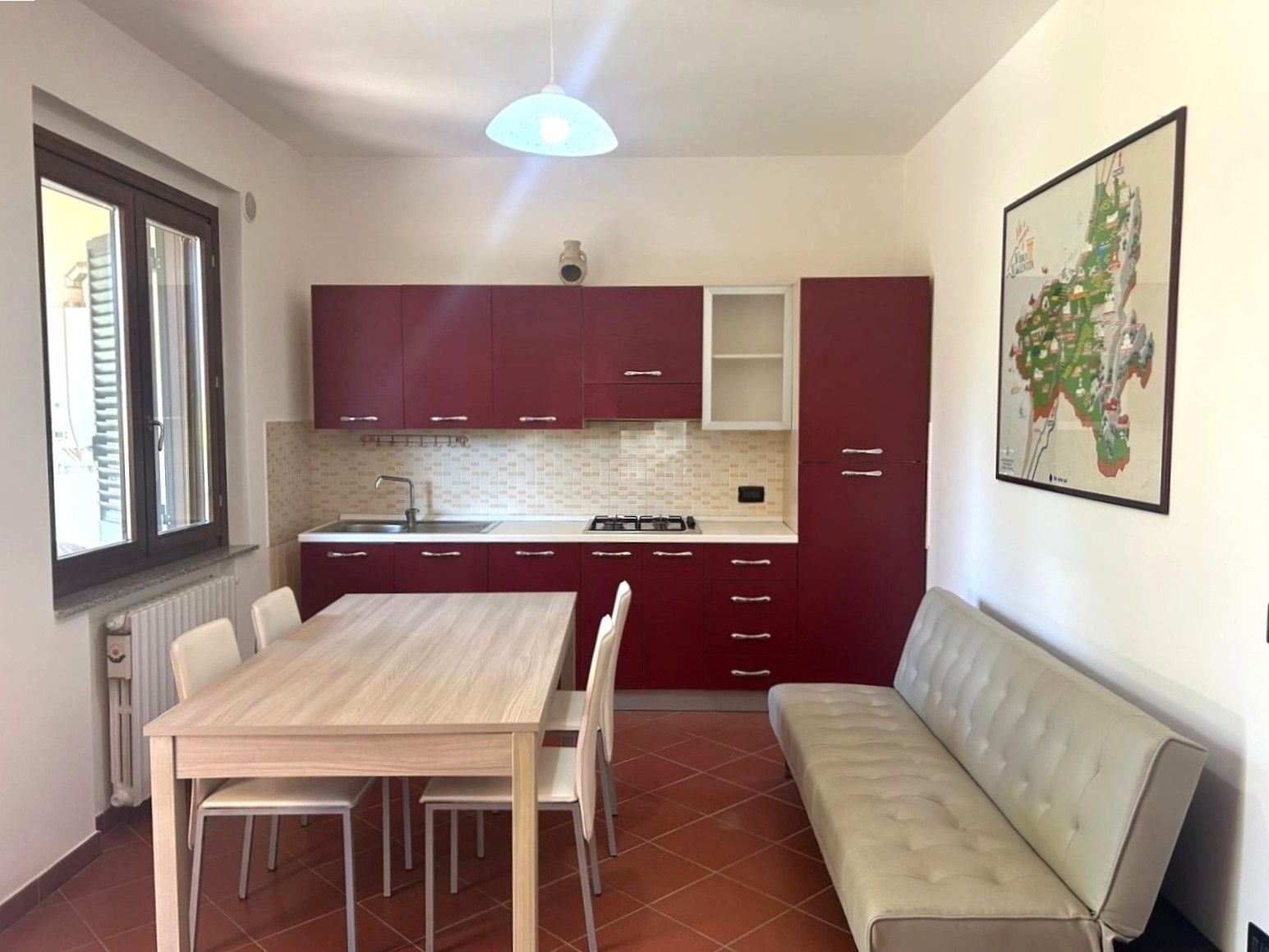 Una cuina compacta amb una taula de dinar i cadires, forn integrat i un armari vermell.