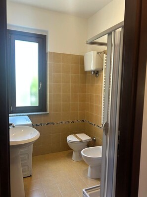 A bathroom with a sink, two toilets, a window, and a shower area.