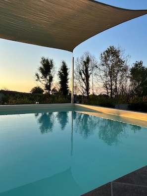 A swimming pool with a clear view of trees and a sunset in the background.