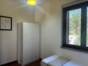Una habitación con cama, armario, ventana y un cuadro en la pared.