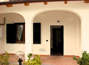 Un edificio con entrada de baldosas, una puerta y una ventana con cortina.