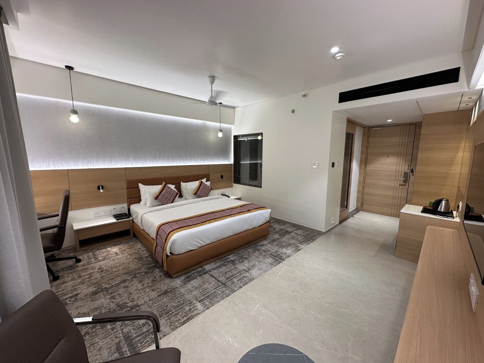 A modern hotel room with a large bed, a desk, and a wardrobe.