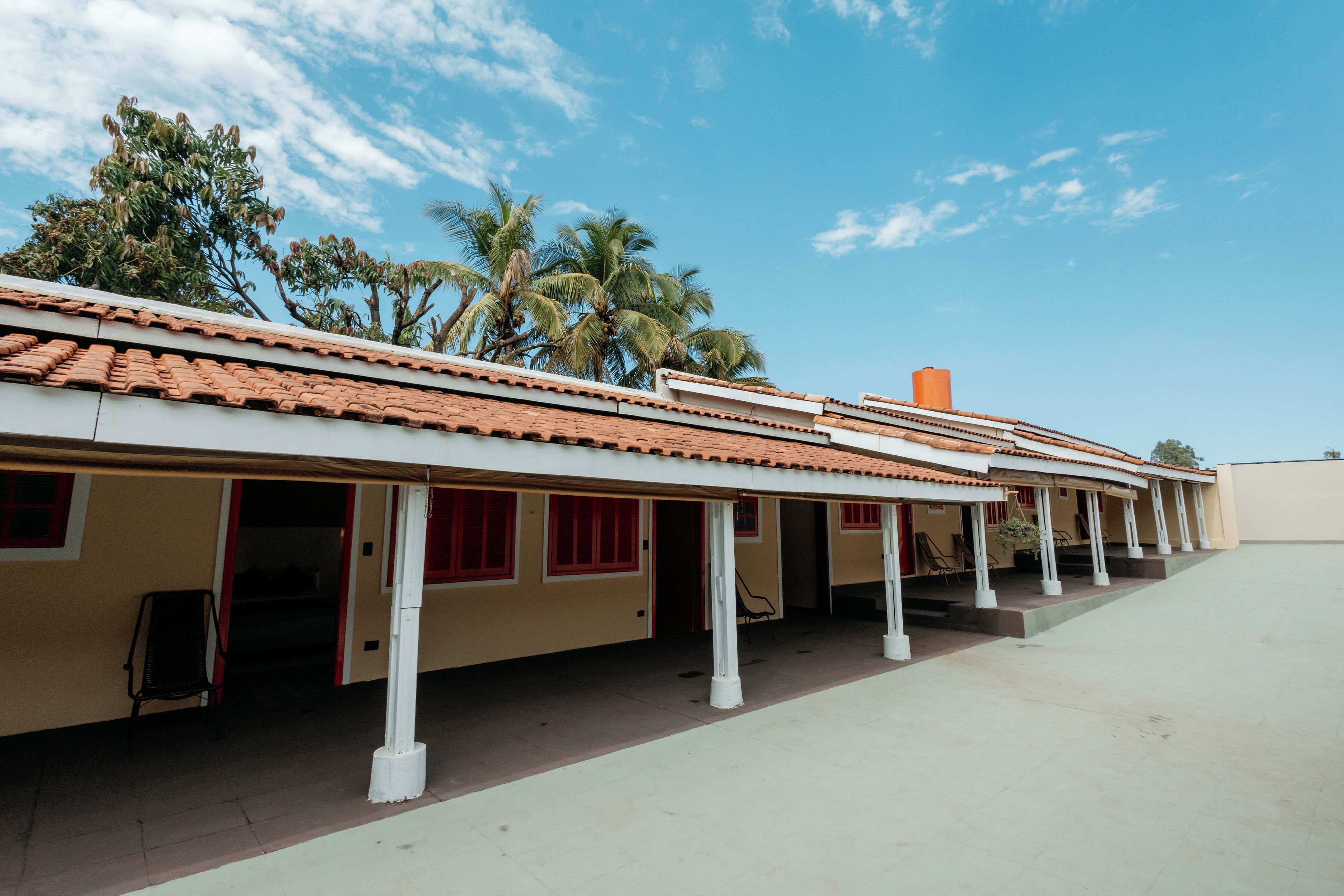 A row of single-story buildings with a tiled roof, white pillars, and red-framed windows.