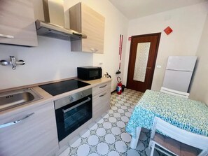 Et kompakt køkken med mikrobølgeovn, ovn, vask og en lille spiseplads med bord og stole.