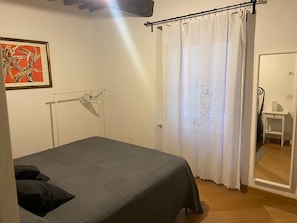 Una stanza con un letto, un appendiabiti, una porta con uno specchio e una parete con un quadro incorniciato.