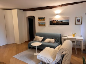 Un accogliente soggiorno con un divano blu, un tavolino rotondo e una poltrona bianca. Si nota un pavimento in legno, una porta bianca e un quadro appeso al muro.