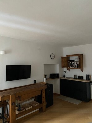 Cocina compacta con televisor de pantalla plana, mesa de madera y microondas.