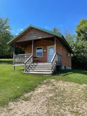 A wooden cabin with a porch, a front door, and a small window. - Ranch Cabin 22 (Portage)